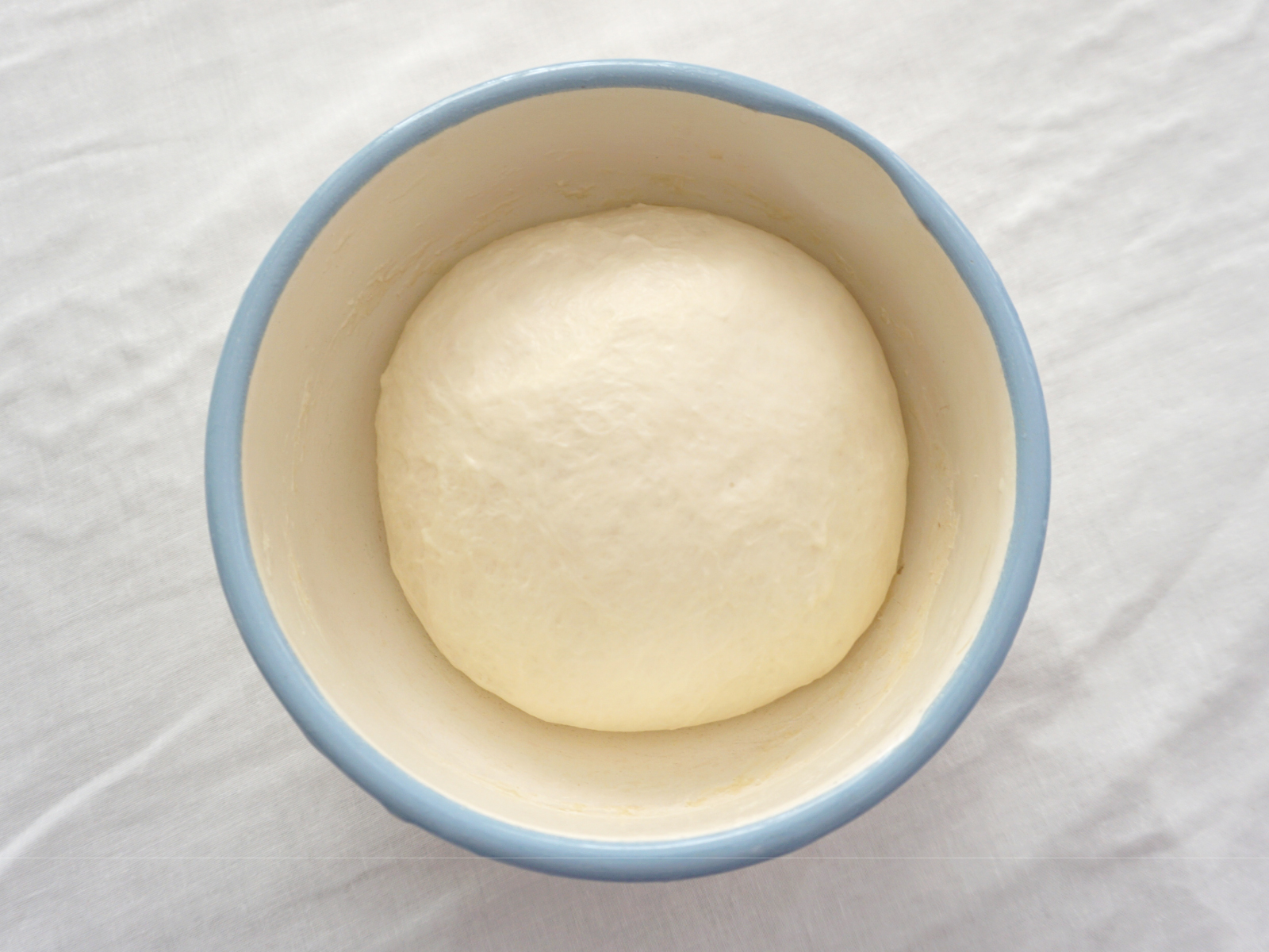 生地が1.5倍くらいまで膨らんだら、テーブルに打ち粉をしたところにだし、手で少しつぶした後、縦に半分折りたたみ、更に横半分に折りたたんでガス抜きする。